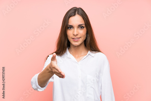 Young woman over isolated pink background handshaking after good deal