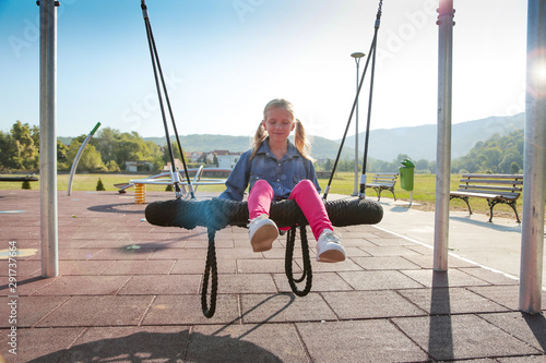 Happy little girl playing on a swing and having fun at kids modern playground