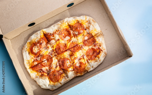 Peperroni pizza in a cardboard box on a blue background. Food delivery concept. Closeup.