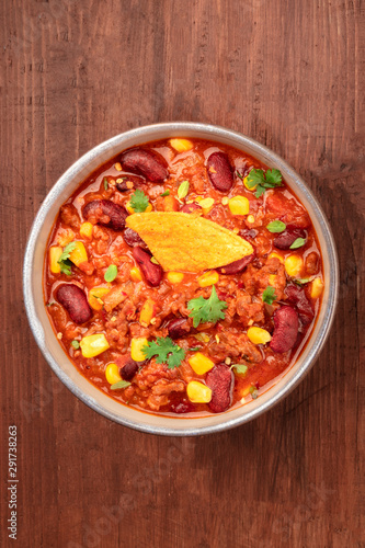 Chili con carne, shot from the top on a dark rustic wooden background with a nacho and copyspace