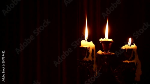 Three candles burn in a candlestick on a black background. Wind blowing on fire. Wax dripped from a burning candle.
