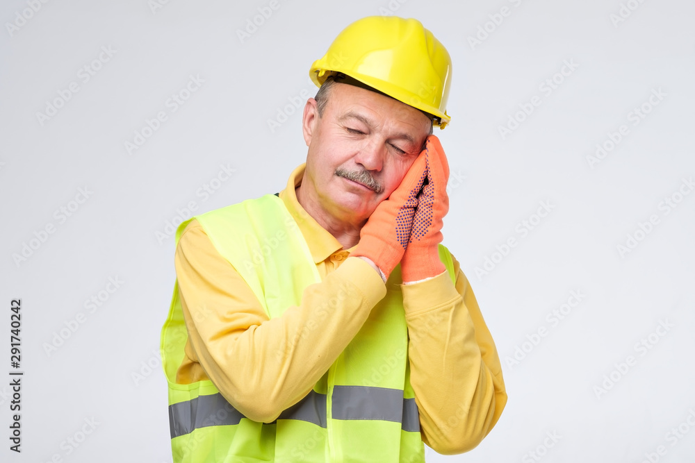 Senior hispanic repairman in yellow helmet is tired and sleepy after hard working day. I need a rest concept. Studio shot Senior hispanic repairman in yellow helmet is tired and sleepy after hard working day. I need a rest concept. Studio shot
