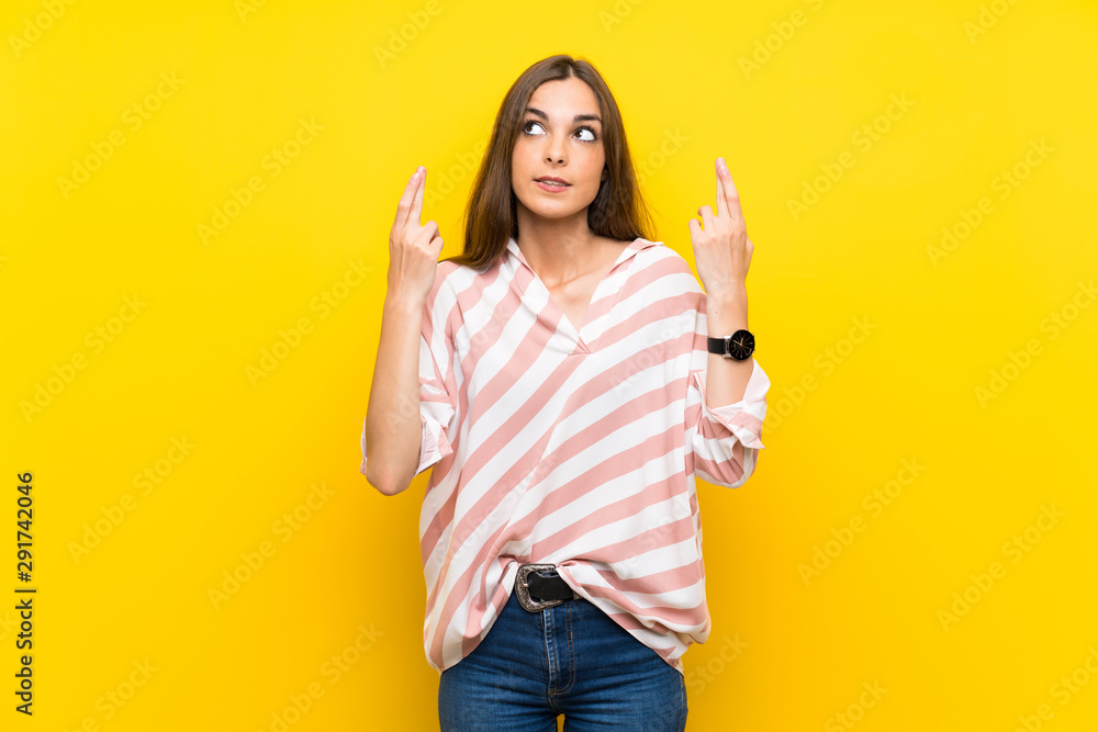 Young woman over isolated yellow background with fingers crossing and wishing the best Young woman over isolated yellow background with fingers crossing and wishing the best