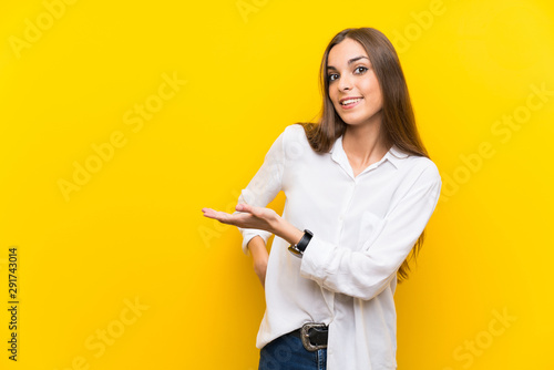 Young woman over isolated yellow background extending hands to the side for inviting to come © luismolinero
