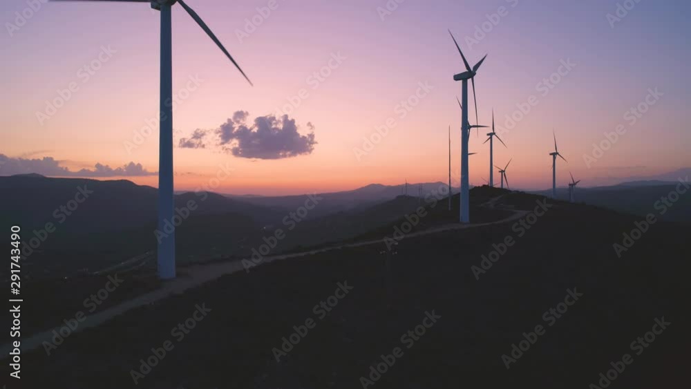 Wind turbines farm silhouettes on beautiful golden hour evening mountain landscape. Renewable energy production for green ecological world. Aerial view of wind mills farm park on evening mountain