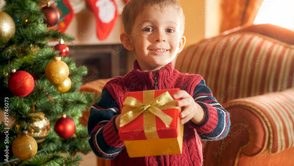 Portrait of little smiling boy giving box with Christmas gift in camera. Perfect image for winter holidays and celebrations