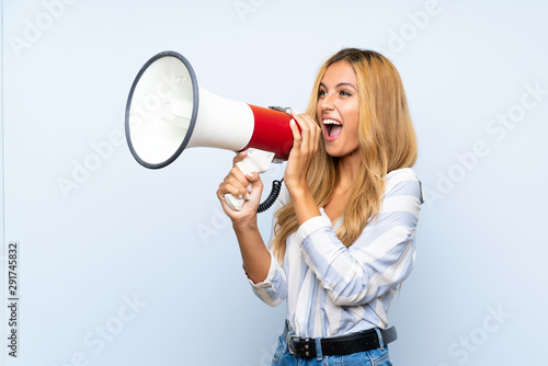 Young blonde woman over isolated blue background shouting through a megaphone