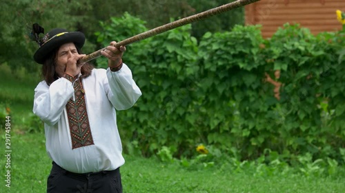 Senior Carpathian man plays trembita instrument. Mature hutsul in traditinal Ukrainian clothing playing trembita. The longest musical instrument. photo