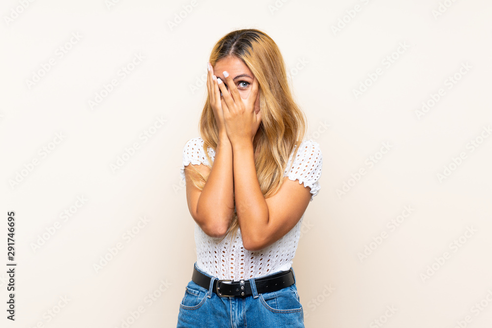 Young blonde woman over isolated background covering eyes and looking through fingers Young blonde woman over isolated background covering eyes and looking through fingers