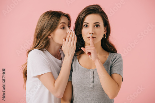 attractive woman telling secret to her friend in t-shirt isolated on pink