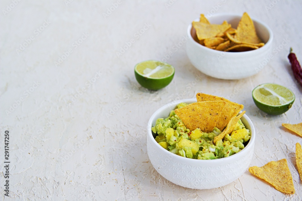 Appetizer, guacamole with mango in a white bowl on a light concrete background. Served with corn chips nachos. Mexican cuisine. Copy space. Appetizer, guacamole with mango in a white bowl on a light concrete background. Served with corn chips nachos. Mexican cuisine. Copy space.