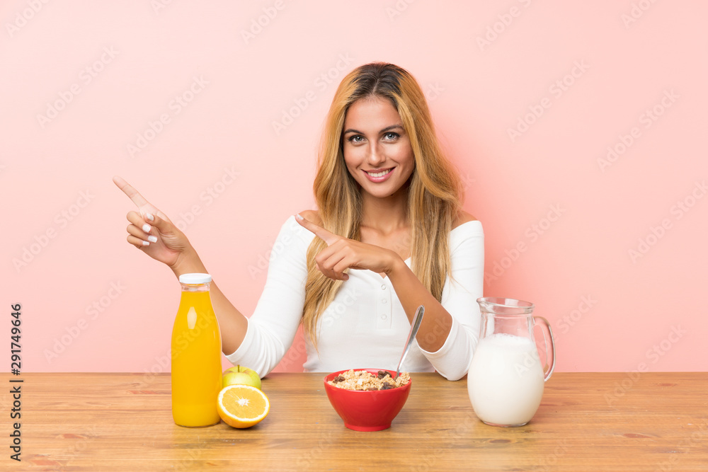 Young blonde woman having breakfast milk pointing finger to the side Young blonde woman having breakfast milk pointing finger to the side