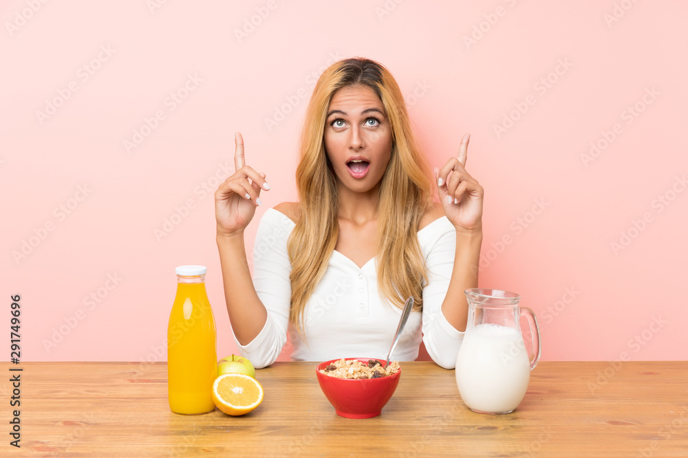 Young blonde woman having breakfast milk pointing with the index finger a great idea Young blonde woman having breakfast milk pointing with the index finger a great idea