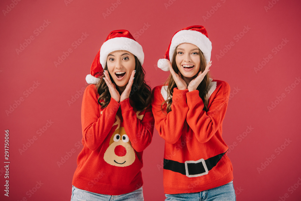 attractive and smiling women in sweaters and santa hats looking at camera isolated on red attractive and smiling women in sweaters and santa hats looking at camera isolated on red