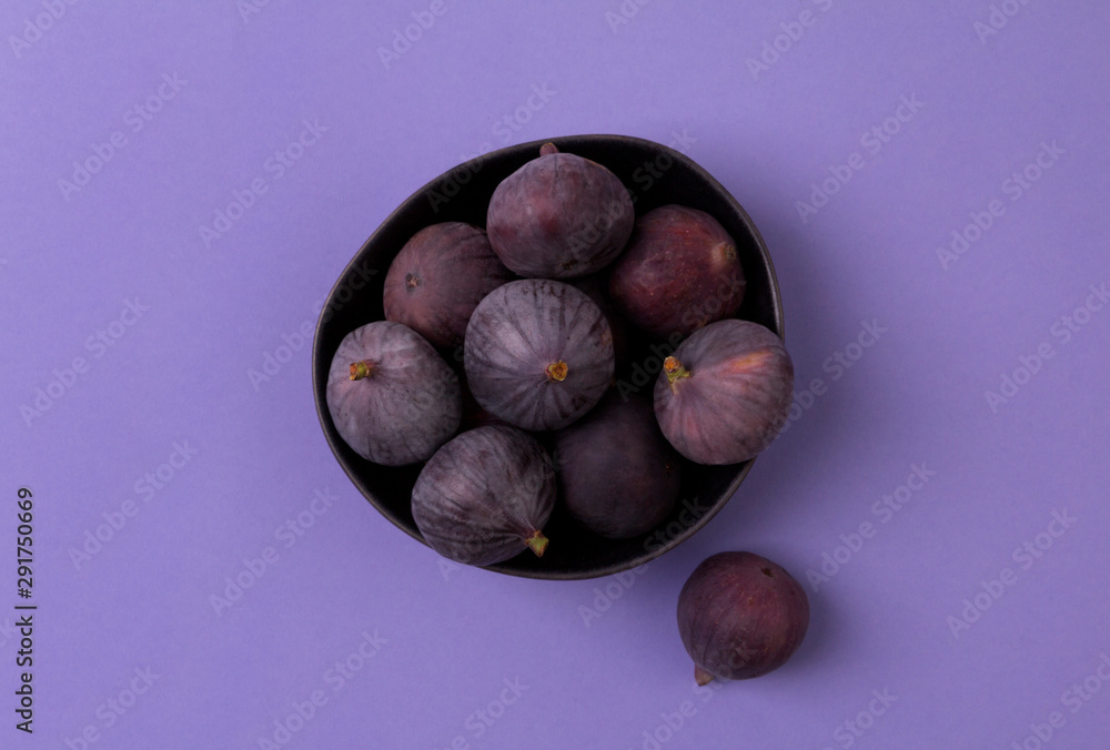 Obraz premium Fresh ripe figs in a bowl close up on a purple background.
