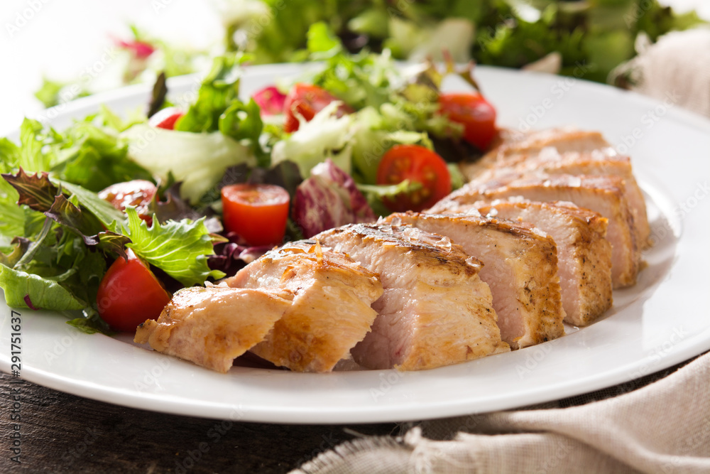 Grilled chicken breast with vegetables on a plate on wooden table. Close up