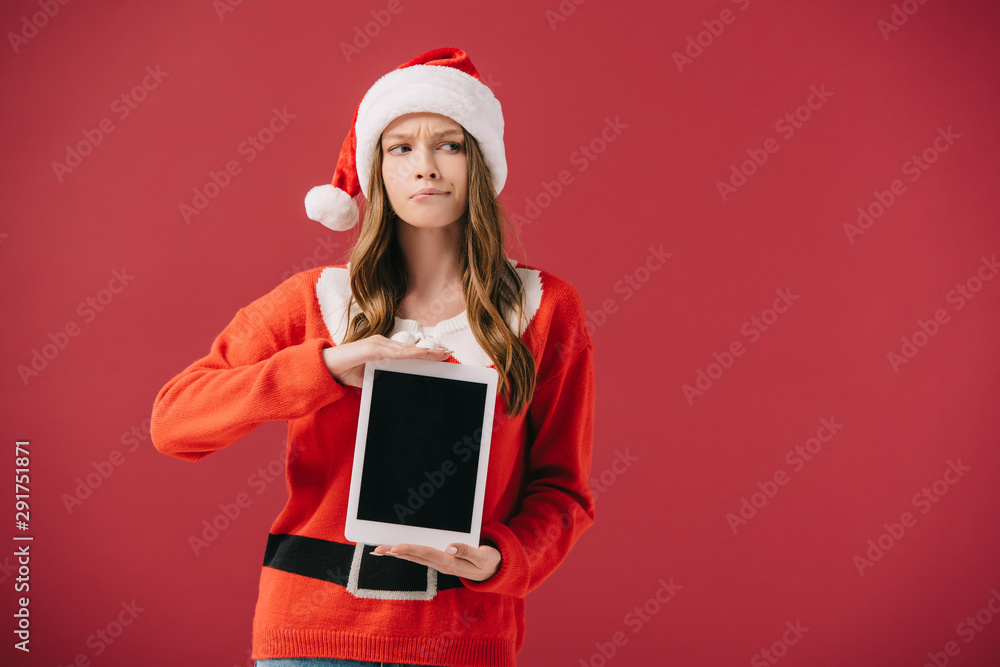 attractive woman in santa hat and sweater holding digital tablet isolated on red attractive woman in santa hat and sweater holding digital tablet isolated on red