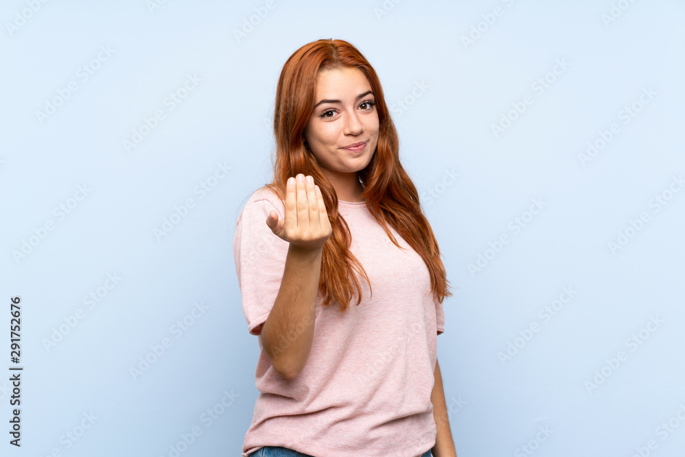 Teenager redhead girl over isolated blue background inviting to come with hand. Happy that you came Teenager redhead girl over isolated blue background inviting to come with hand. Happy that you came