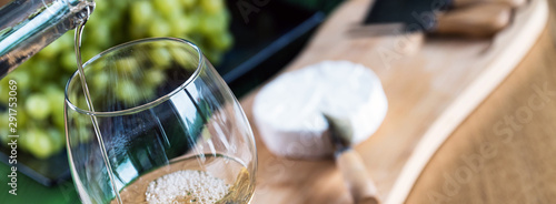 Pouring white wine into the glass against wooden background