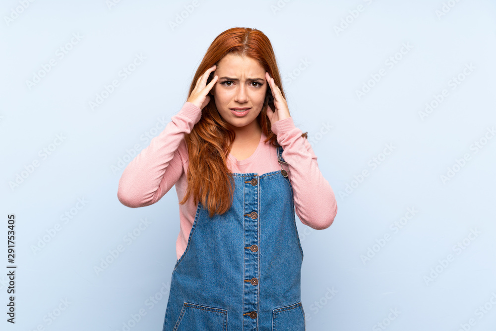 Teenager redhead girl with overalls over isolated blue background unhappy and frustrated with something. Negative facial expression Teenager redhead girl with overalls over isolated blue background unhappy and frustrated with something. Negative facial expression