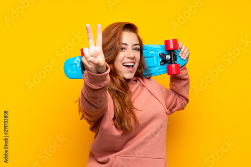 Teenager redhead girl with skate making victory gesture over isolated yellow background