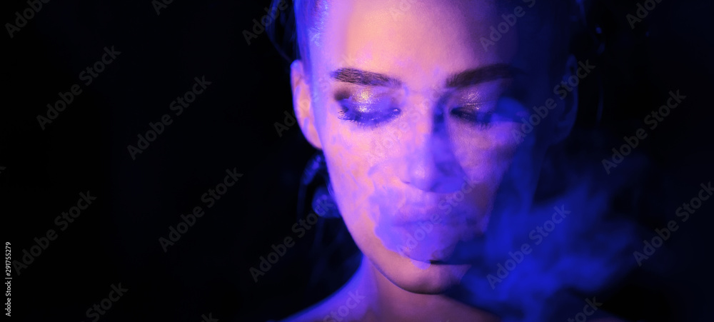 Woman smoking e-cigarette in blue neon light in dark studio Woman smoking e-cigarette in blue neon light in dark studio