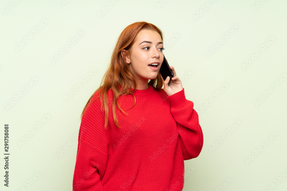 Teenager redhead girl with sweater over isolated green background using mobile phone Teenager redhead girl with sweater over isolated green background using mobile phone