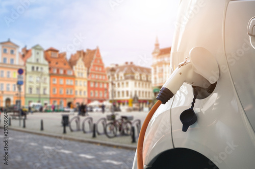 Close up of electric car with a connected charging cable on the blurred background of a european city 