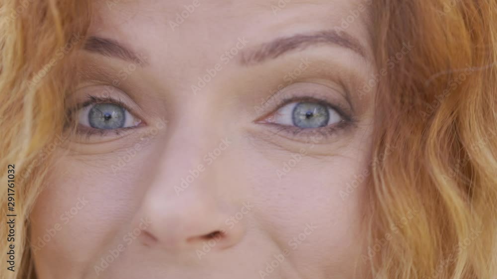 Close-up face of pretty mature red-haired woman with curly hair smiling happily looking at the camera in the park. Emotions, happiness, good mood Close-up face of pretty mature red-haired woman with curly hair smiling happily looking at the camera in the park. Emotions, happiness, good mood