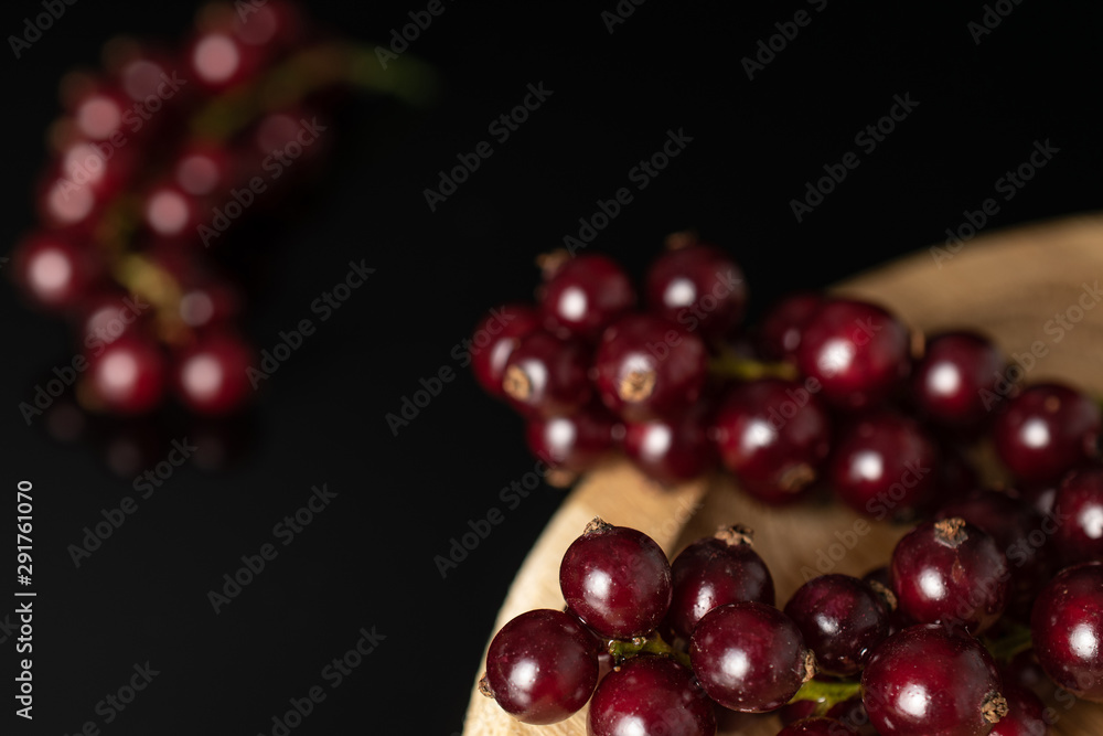 Lot of whole fresh dark redcurrant closeup on bamboo plate isolated on black glass Lot of whole fresh dark redcurrant closeup on bamboo plate isolated on black glass