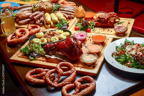 Flat-lay of Oktoberfest dinner table with grilled meat sausages, pretzel pastry, potatoes, cucumber salad, sauces, beers photo