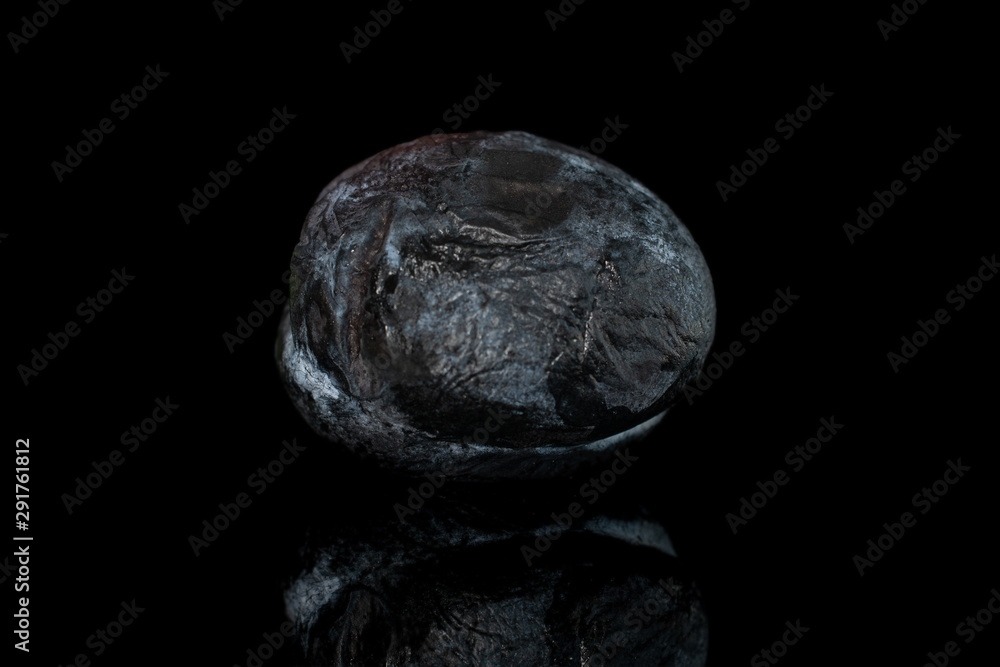 One whole drying dark blue plum isolated on black glass One whole drying dark blue plum isolated on black glass