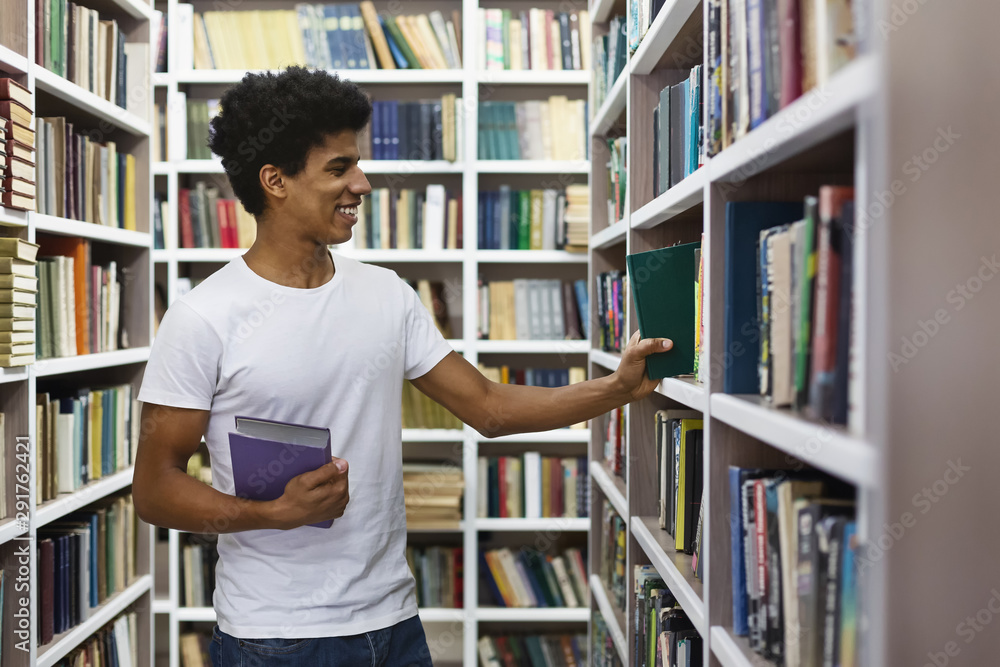 Handsome black guy looking for book on bookshelves in library Handsome black guy looking for book on bookshelves in library