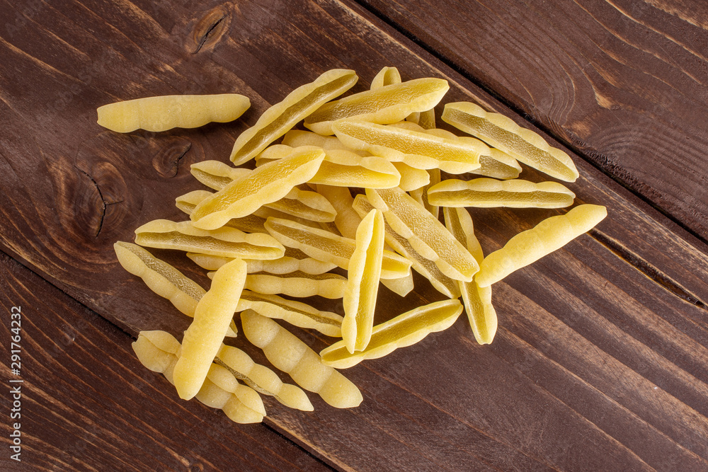 Lot of whole uncooked pasta cavatelli heap flatlay on brown wood Lot of whole uncooked pasta cavatelli heap flatlay on brown wood