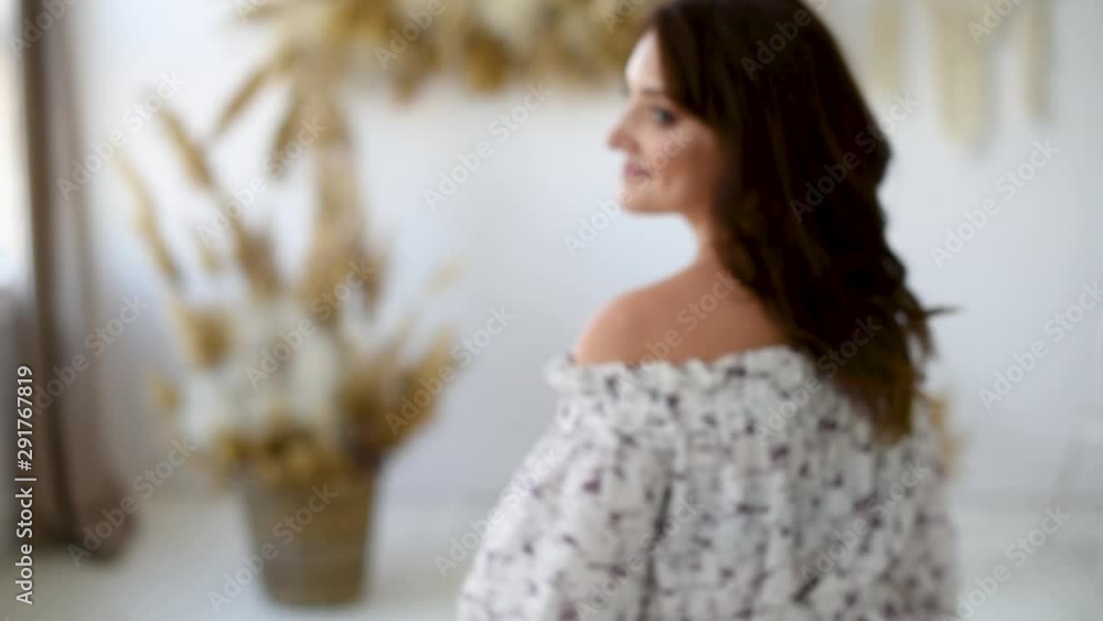Smiling  attractive brunette woman with long hair in dress walking to unfocused in room with spikes