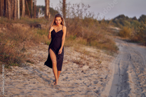 girl in a black evening dress walks along the shore of a forest lake at sunset on an autumn day