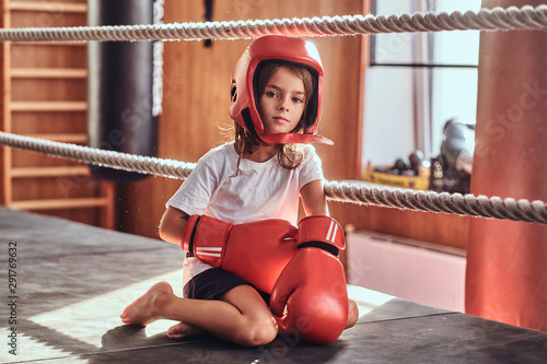 Sportive young girl is sitting on sunny ring wearing her eguipment - helmet and boxing gloves. photo