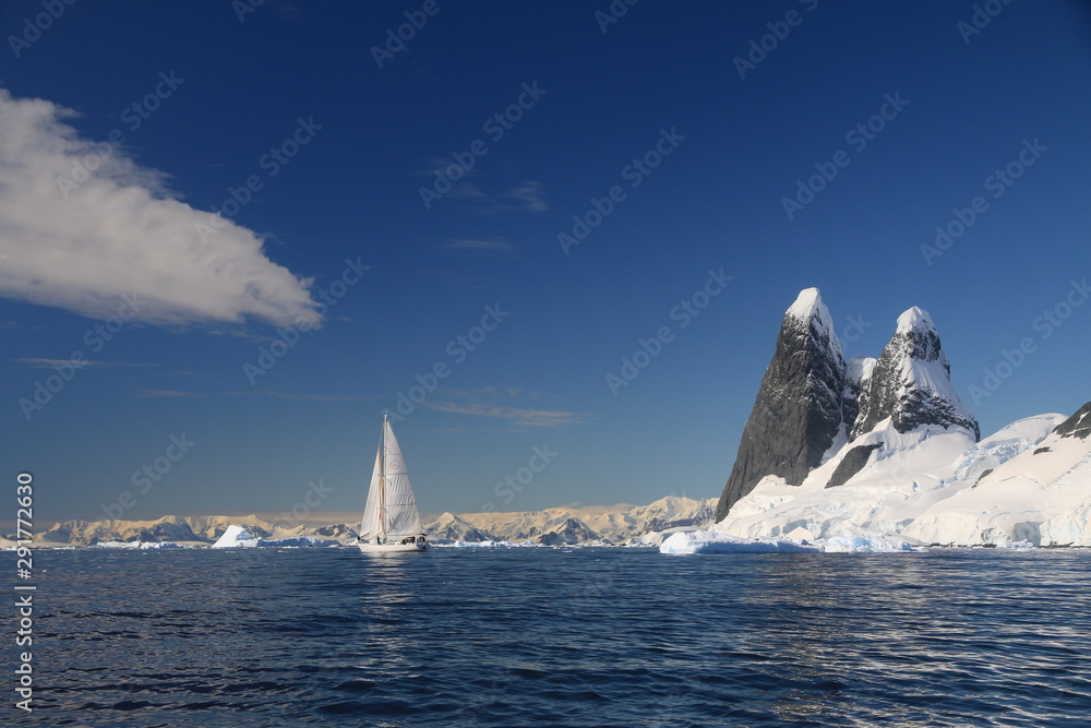 jacht z rozłożonymi żąglami na zimnych wodach okołobiegunowych z antarktydą w tle w słoneczny dzień