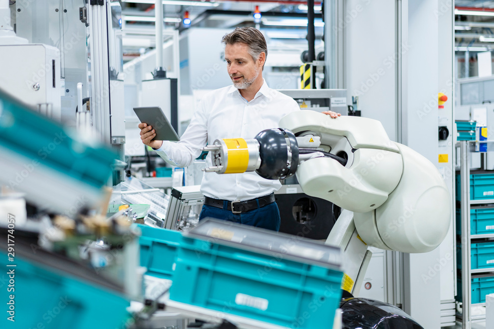Businessman with tablet at assembly robot in a factory