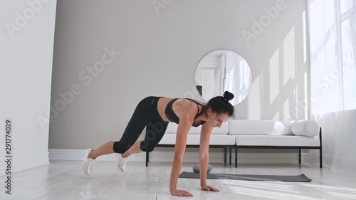 Beautiful slim woman in thirties with fair complexion does morning strenth and aerobic burpee exercises in modern airy room. photo