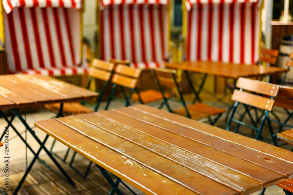 View to a group of wooden patio furniture on the terrace of a restaurant with three unfocussed beach chairs in the background. View to a group of wooden patio furniture on the terrace of a restaurant with three unfocussed beach chairs in the background.