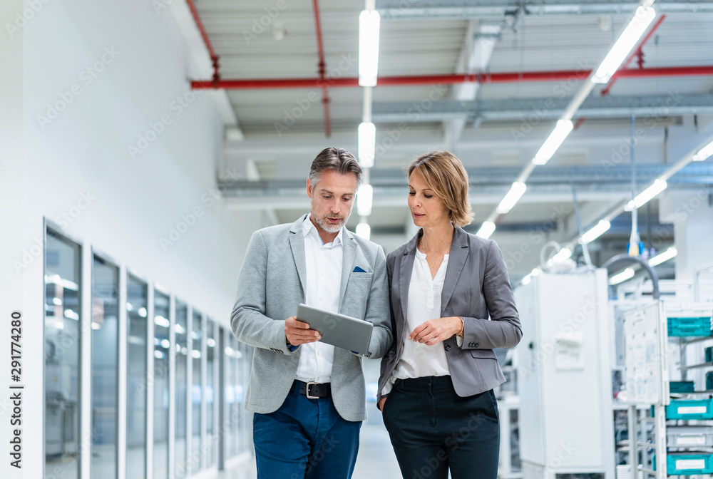 Businesswoman and businessman with tablet walking and talking in a modern factory Businesswoman and businessman with tablet walking and talking in a modern factory