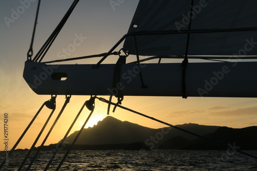 kontury lądu i zachód słońca widziane zza elementów wyposażenia płynącego jachtu