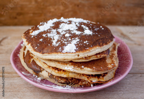 Stack of homemade clean eating oat pancakes with powered sugar on pink plate on rustic country table. Selective soft focus. Shrovetide, pancake carnival maslenitsa concept