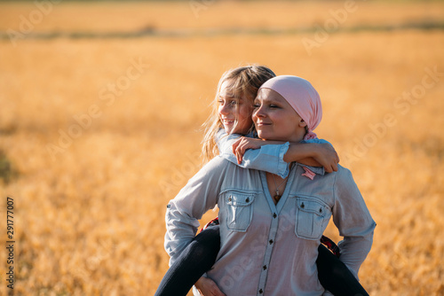 A woman with cancer carrying her daughter on her back, looking sideways photo