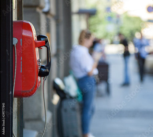 Red street phone on a blurred sidewalk background with walking people in St. Petersburg.