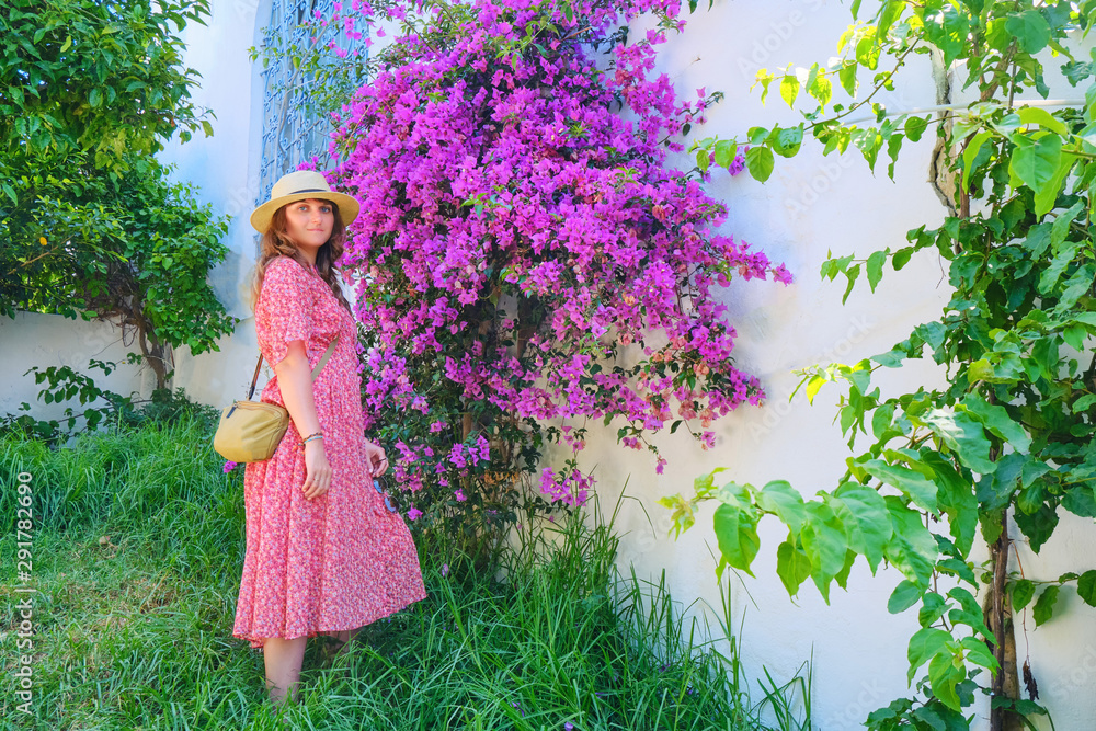 A woman in a straw hat next to purple flowers on a large Bush in Sidi Bou Said, Tunisia
