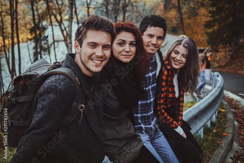 Group of good friends have fun while sitting on the side road at autumn forest.