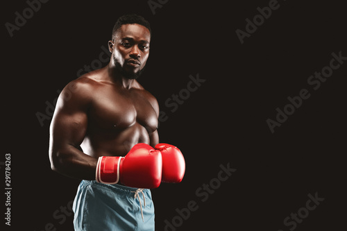 Athletic fighter with red gloves on posing over black background
