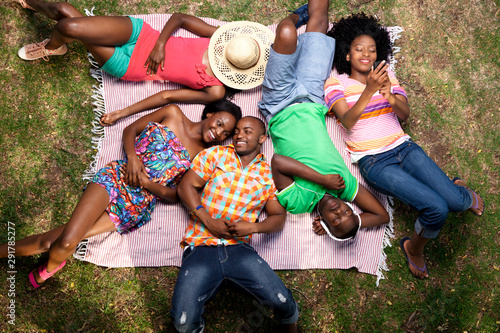 Shot from above of five young black friends lying on a blanket in a park, looking up and smiling photo